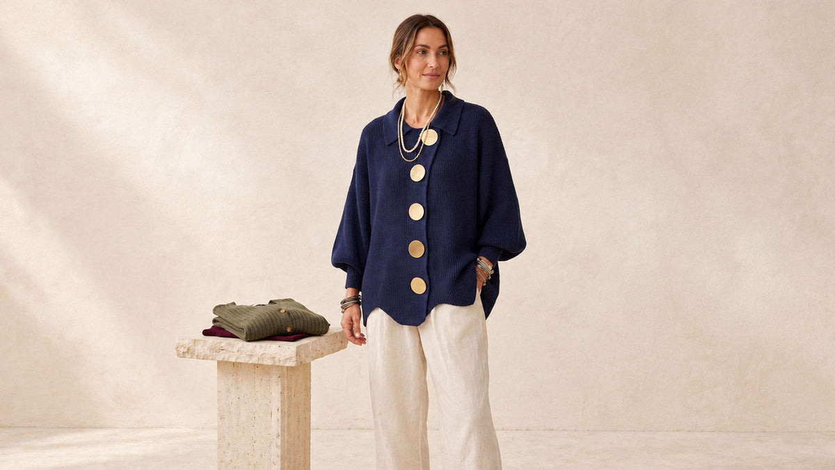 Woman wearing a navy button-front cardigan, centered beside folded knitwear.
